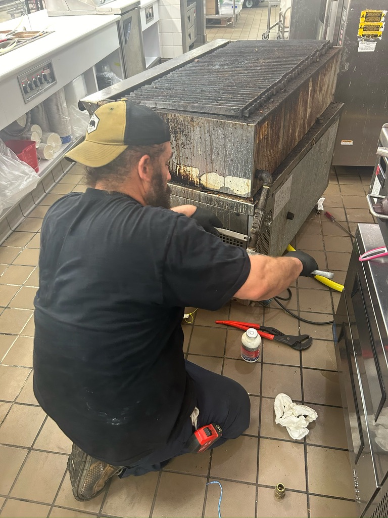 Northmark Plumbing technician repairing the gas connection on a commercial charbroiler in a restaurant kitchen